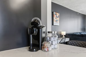 A modern living room with a coffee machine, a glass jar with spices, and a framed artwork on the wall. - The Concord - Modern Condo Downtown YXE (Saskatoon)