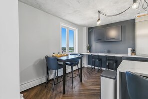 Eine moderne Küche mit Essbereich, ausgestattet mit einem großen Fenster, dunklen Schränken und einer Marmorarbeitsplatte.