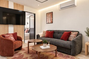 A modern living room with a sofa, armchair, coffee table, and a flat-screen TV mounted on the wall. - TheBlueStay 366 - Beautiful A/C Apartment in Paris (Paris)