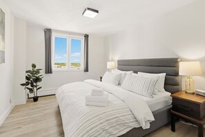 Une chambre d’hôtel avec un lit, des tables de chevet, une lampe, une plante en pot et une fenêtre avec des rideaux.