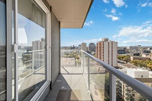 Un balcon avec vue sur la ville, de grandes fenêtres et une rambarde en métal.