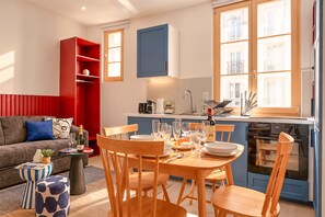 Een moderne woonkamer met een bank, een eettafel gedekt voor vier personen en een keuken met een kookplaat en kasten.