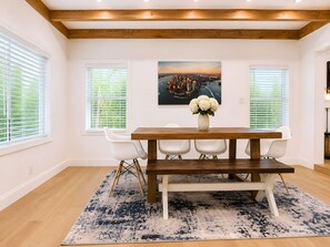 Een eethoek met een houten tafel, witte stoelen en een blauw tapijt met patroon.