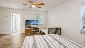 A bedroom with a bed, a TV on a stand, a ceiling fan, a window with blinds, and a door leading to another room. - Your Perfect Fort Lauderdale Stay I 4BR, Private Pool & Free Parking (Fort Lauderdale)