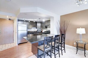 Een moderne keuken met roestvrijstalen apparatuur, een groot eiland met barstoelen en een eethoek met een lamp.