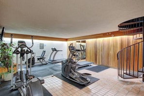 Ein Fitnessstudio mit unterschiedlichen Trainingsgeräten, darunter Laufbänder und Ergometer, sowie eine Holzwand mit Spiegel.
