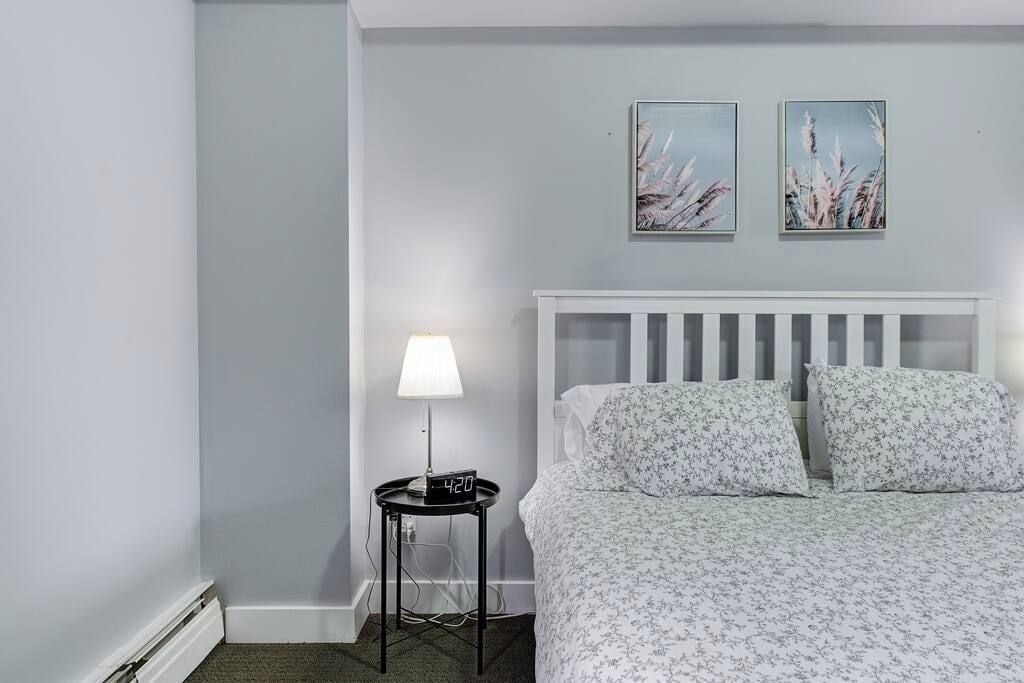 A bedroom with a bed, a nightstand with a lamp, and two wall-mounted pictures.