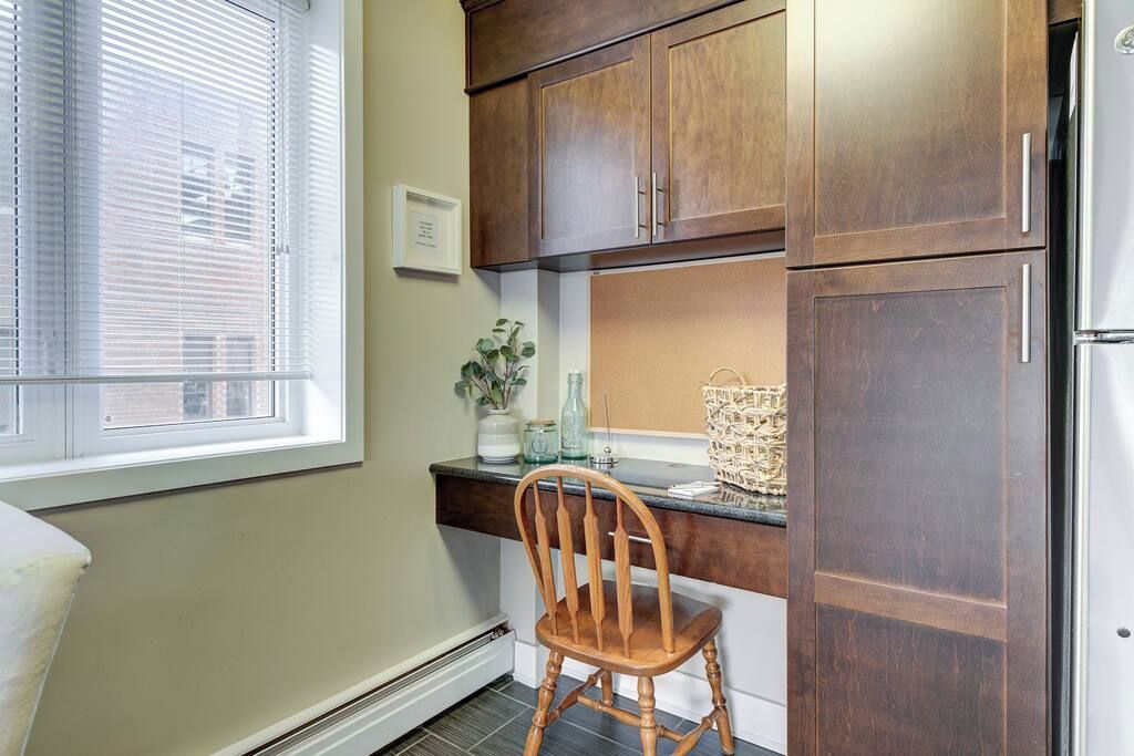 A kitchen with wooden cabinets, a white refrigerator, a window with blinds, and a chair.