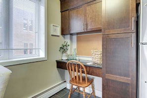 Une cuisine avec des meubles de rangement en bois, un réfrigérateur blanc, une fenêtre avec des stores et une chaise.