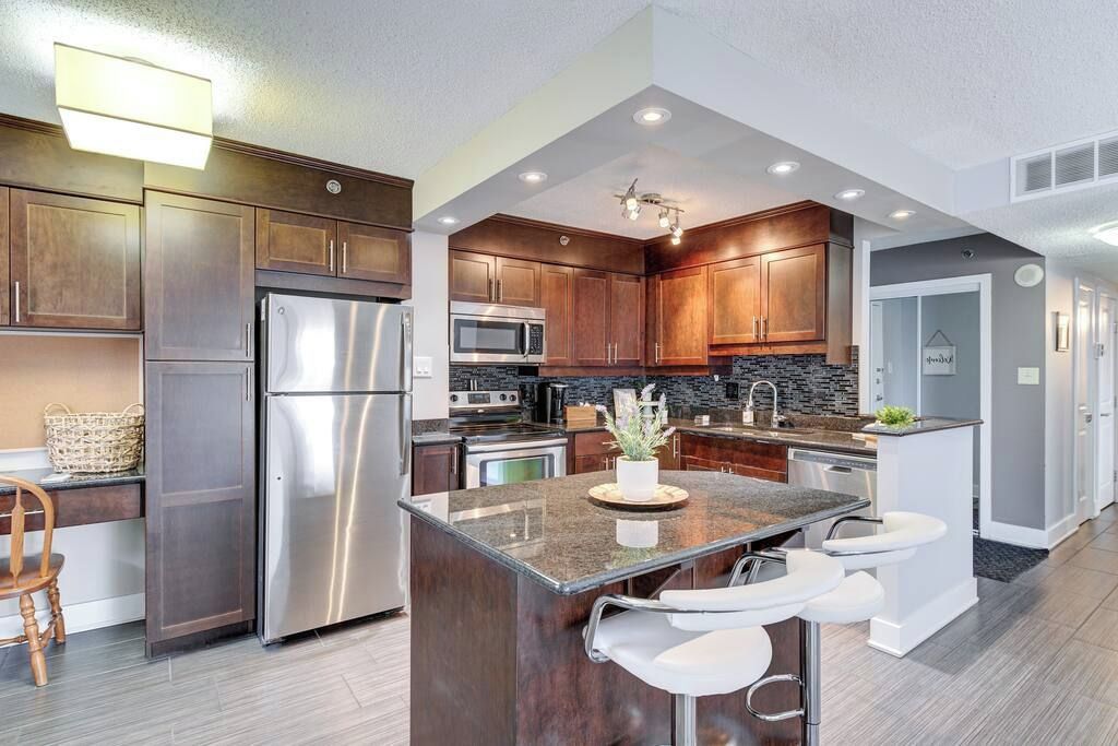 A modern kitchen with dark wood cabinets, stainless steel appliances, and a central island with bar stools.