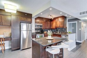 Une cuisine moderne avec des meubles en bois foncé, des appareils électroménagers en acier inoxydable et un îlot central doté de tabourets de bar.