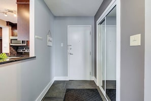 Un couloir avec une porte, un coin cuisine avec des placards et des appareils électroménagers, et un tapis sur le sol.