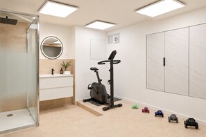 A modern bathroom with a glass shower enclosure, a round mirror, a wall-mounted toilet, and a small exercise area with dumbbells. - TheBlueStay 369 - Beautiful A/C Apartment in Paris (Paris)