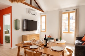 A dining area with a table set for two, a television mounted on the wall, and a window with curtains. - TheBlueStay 369 - Beautiful A/C Apartment in Paris (Paris)