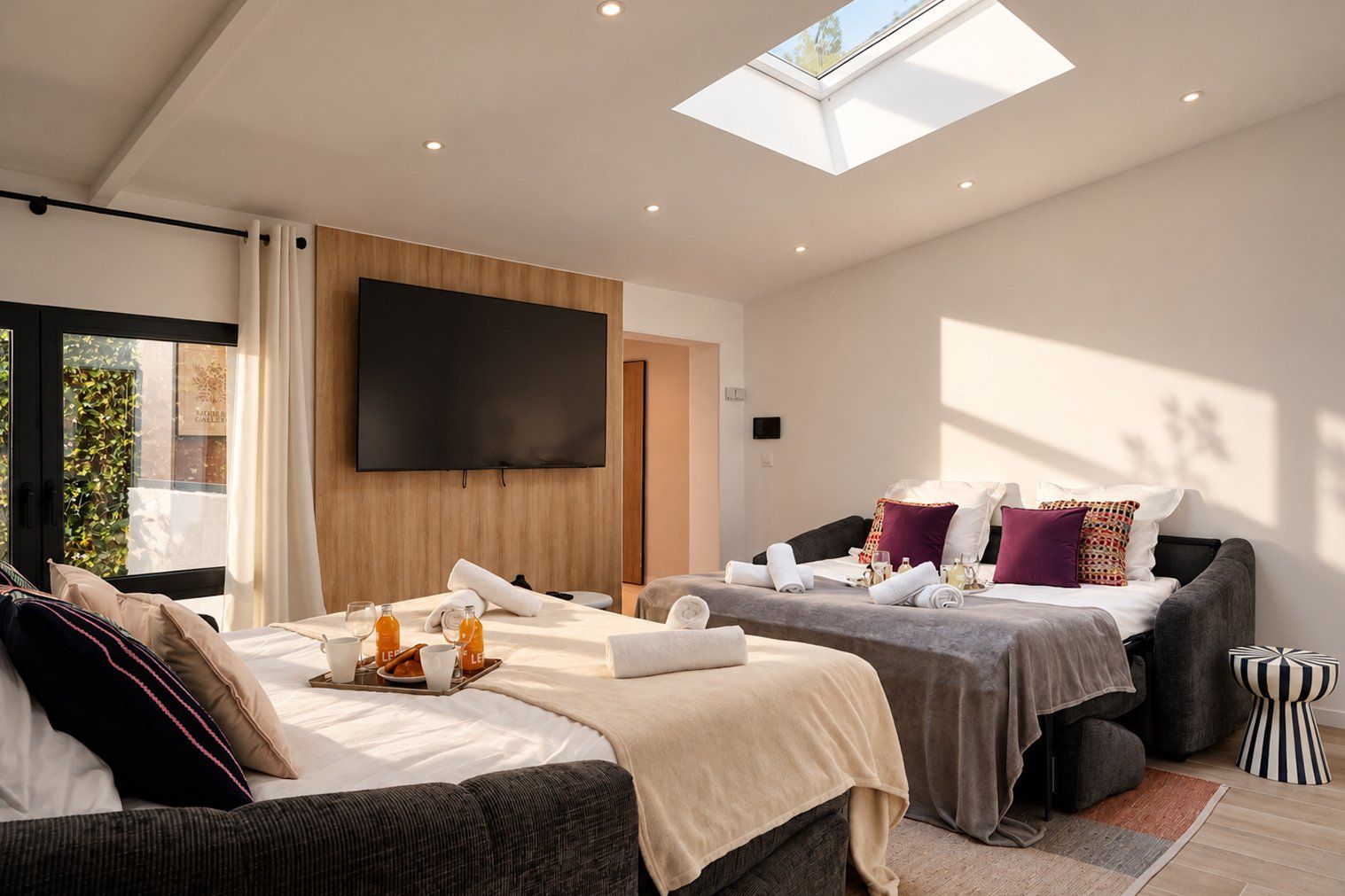 A modern hotel room with a large bed, a smaller bed, a flat-screen TV, and a skylight.
