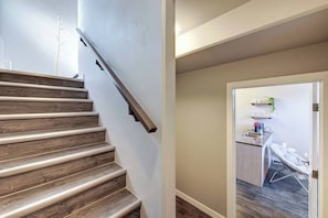 A staircase with wooden steps and a handrail, leading to a room with a kitchen area visible through an open door.