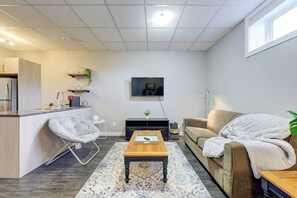 Un espacio habitable compacto con kitchenette, un sofá, una mesa de centro y un televisor de pantalla plana montado en la pared.