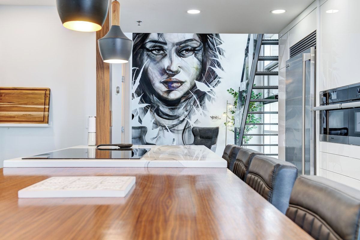 Une cuisine moderne agrémentée d’une grande fresque murale, d’une table à manger en bois et d’un four encastré.