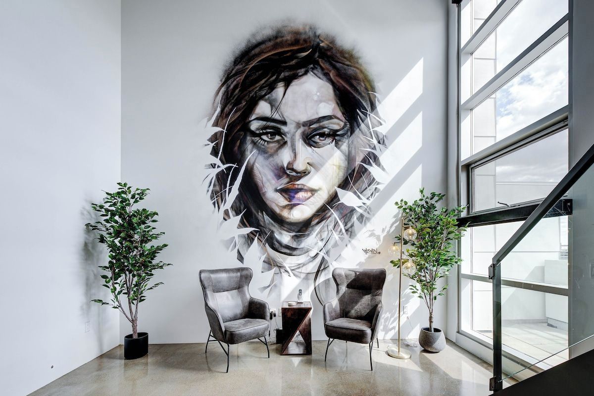 A modern interior with a large abstract mural, two armchairs, and potted plants.