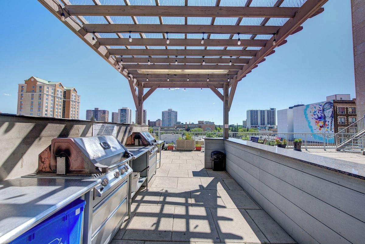 An outdoor patio with a pergola, barbecue grill, and a view of a cityscape.