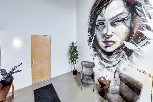 Un intérieur moderne agrémenté d’une grande fresque murale, d’une porte en bois, d’une plante en pot et de deux fauteuils.