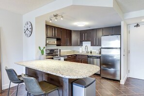 A modern kitchen with granite countertops, stainless steel appliances, and dark cabinetry. - The Tuscany - Located Downtown! (Saskatoon)