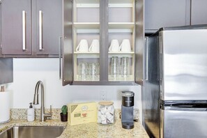 A kitchen with a stainless steel refrigerator, a built-in cabinet with cups and glasses, a coffee maker, and a jar of tea. - The Tuscany - Located Downtown! (Saskatoon)