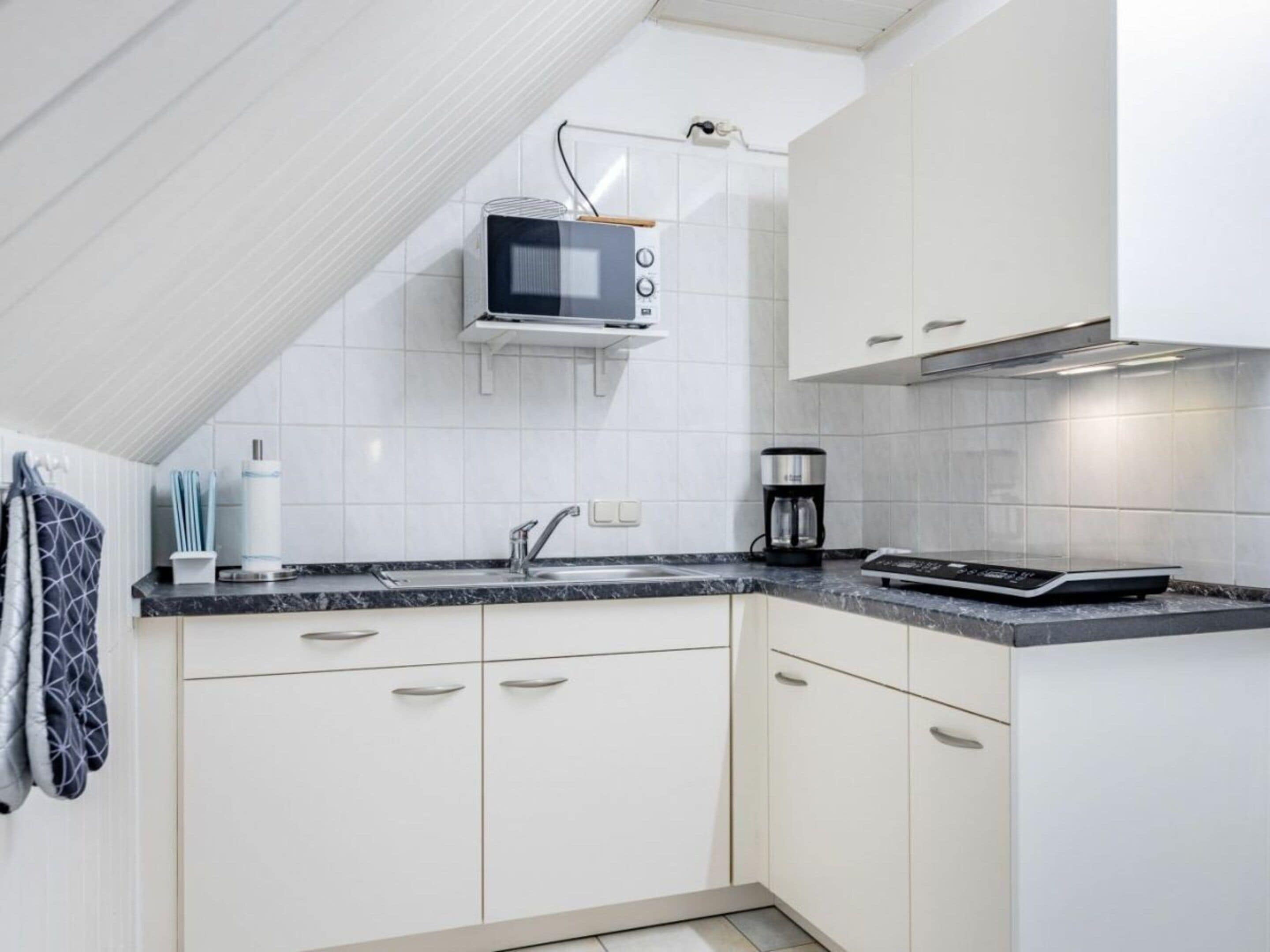 A modern kitchen with white cabinets, a microwave, a coffee maker, and a built-in oven.