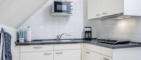 Una cocina moderna con armarios blancos, microondas, cafetera y horno integrado.