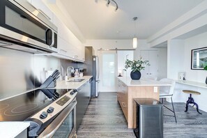 Eine moderne Küche mit Edelstahlgeräten, einer zentralen Kochinsel und einem Essbereich mit einem weißen Stuhl und Tisch.