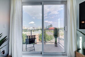 Ein Zimmer mit einer großen Schiebeglasdoor zum Balkon, auf dem ein Sessel und ein Blumentopf stehen.