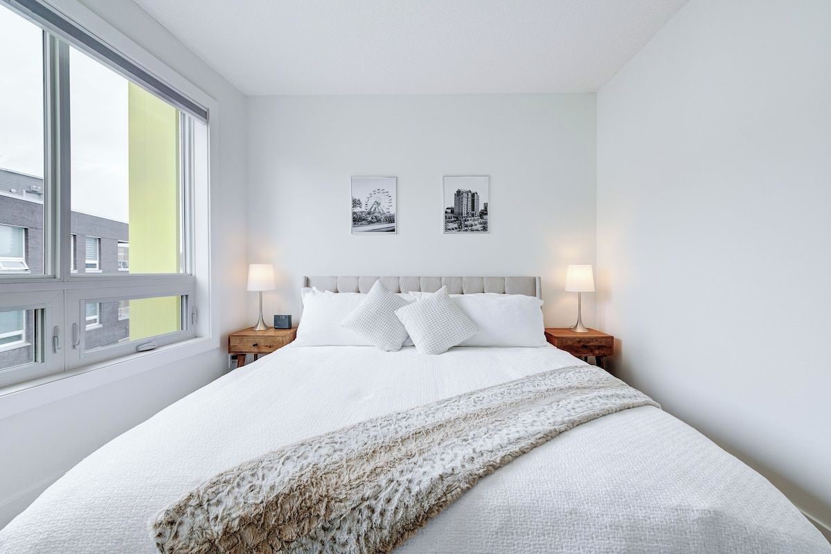 A hotel room with a large bed, two bedside tables, a window, and two wall-mounted pictures.
