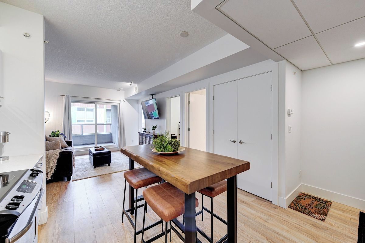 A modern kitchen with a wooden table, bar stools, and a built-in oven.