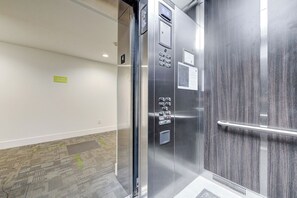 Un ascenseur avec une finition métallique, un panneau de commande et une barre d’appui.