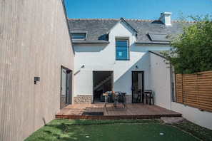 Uma casa moderna com um deck de madeira, um pequeno pátio e céu claro.