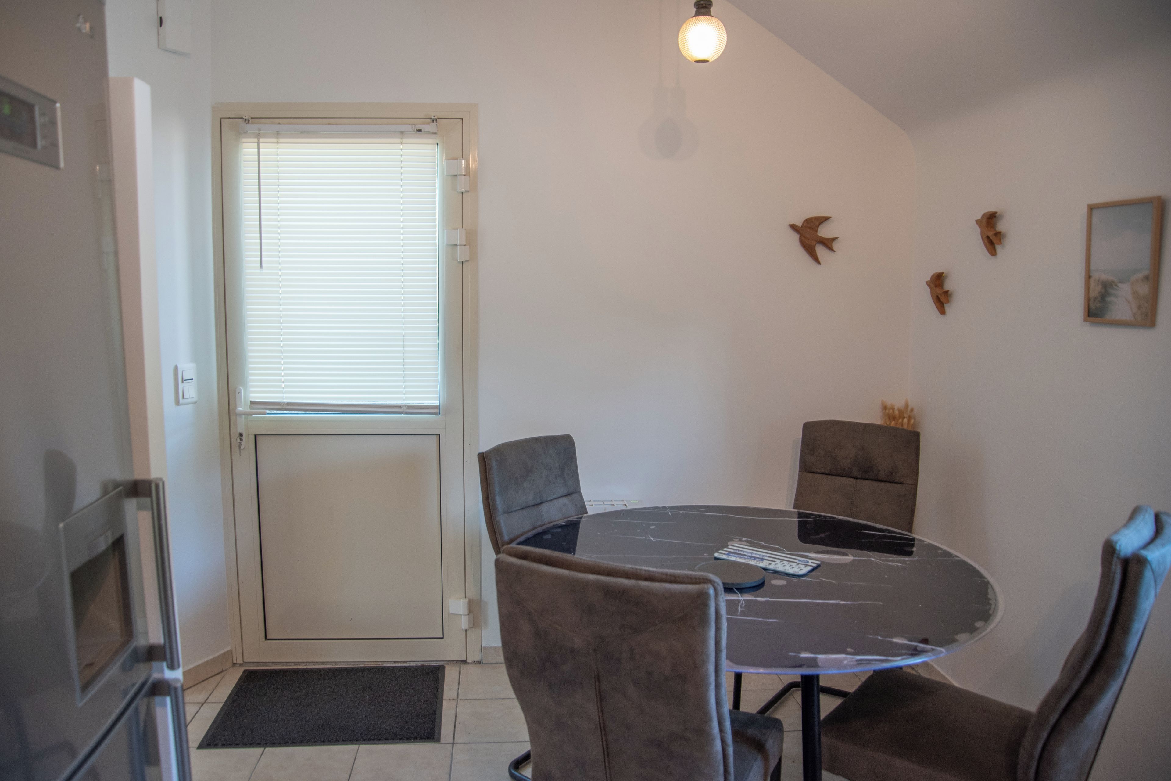 Ein Zimmer mit einem runden Tisch, vier Stühlen, einer Tür mit Fenster und einer Leuchte.