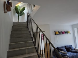Una escalera con barandilla de metal que conduce a una plataforma, una planta en maceta y un estante con adornos.