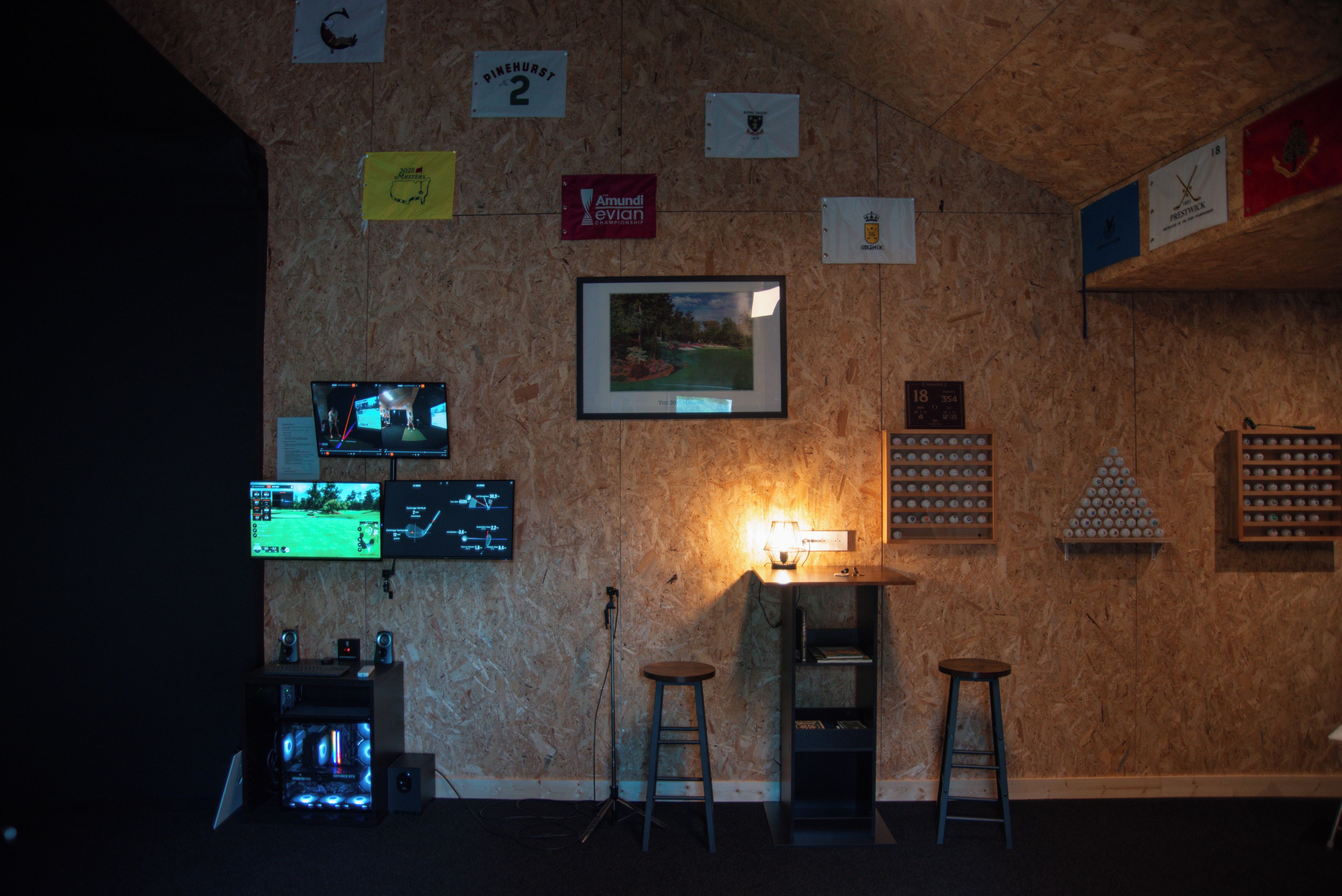 Ein Zimmer mit einer Holzwand, mehreren Bildschirmen, einem gerahmten Bild und einem Regal mit Golfbällen.