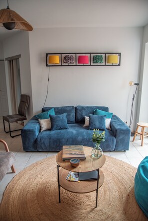A modern living room with a blue-striped sofa, a round coffee table with a book and vase, and a wall-mounted lamp.