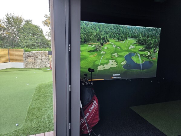 A golf course view on a screen, a golf bag, and a stone wall.