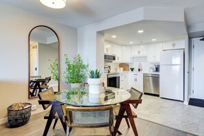 A modern kitchen with white cabinets, stainless steel appliances, and a dining area with a glass table and wicker chairs. - The Frederick - UG Parking! (Saskatoon)