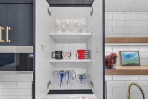 A kitchen with a white cabinet containing wine glasses, mugs, and glassware. - The Nest - Cozy 1BR | Free Parking (Saskatoon)