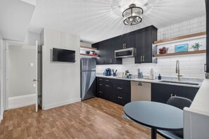 A modern kitchen with dark cabinetry, a stainless steel refrigerator, a microwave, and a sink. - The Nest - Cozy 1BR | Free Parking (Saskatoon)