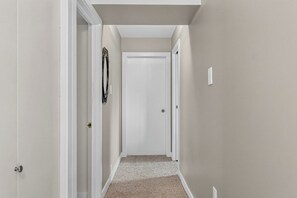 A narrow hallway with white walls and carpeted flooring, leading to a closed door at the end. - The Nest - Cozy 1BR | Free Parking (Saskatoon)