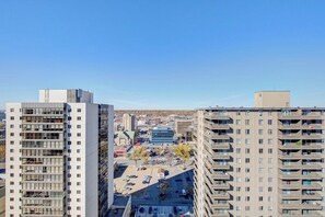 A high-rise building with multiple floors, a parking lot in the foreground, and a clear sky. - Metro | Parking, Gym, Rooftop Patio (Saskatoon)