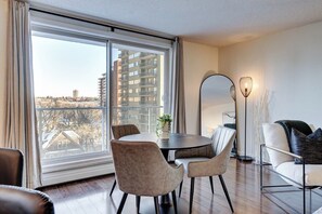 A modern living room with a large window, a round dining table, and a sofa. - Metro | Parking, Gym, Rooftop Patio (Saskatoon)