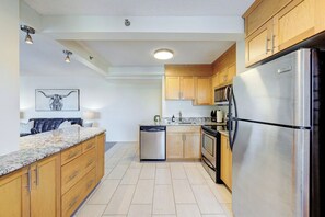 A modern kitchen with wooden cabinets, a stainless steel refrigerator, a dishwasher, and a granite countertop. - Metro | Parking, Gym, Rooftop Patio (Saskatoon)