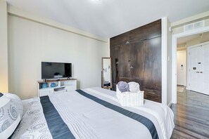 A hotel room with a large bed, a television, a wardrobe, and a bathroom visible through an open door. - The Oslo - 2BD Downtown (Saskatoon)
