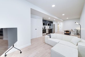 A modern living room with a sectional sofa, a flat-screen TV, and a dining area with a table and chairs.