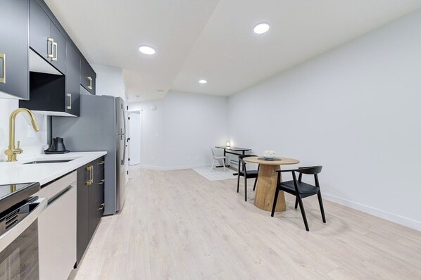 A modern kitchen with a dining area, featuring a sink, stove, and a round table with chairs.